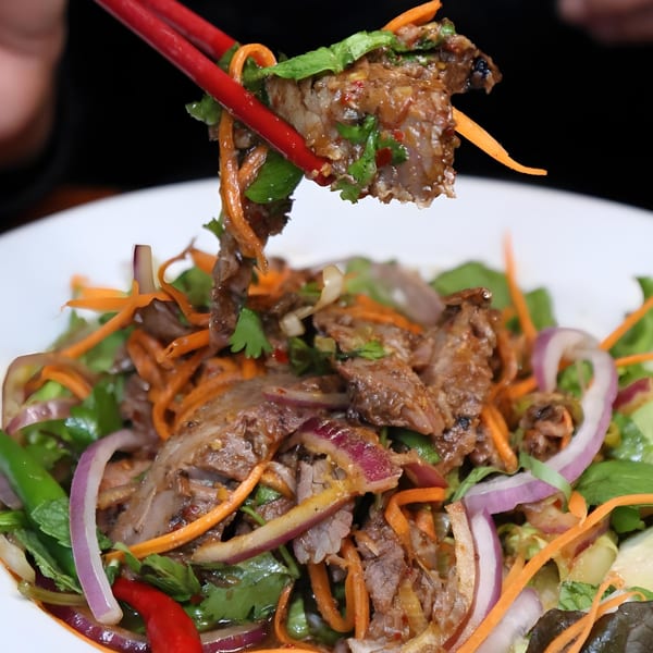 Red chopsticks lifting a piece of beef from a B & K Asian Kitchen salad with vegetables.