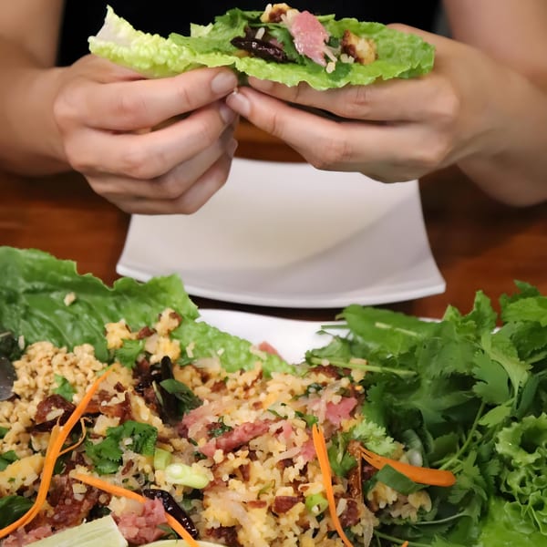 Hands holding a lettuce wrap filled with B & K Asian Kitchen's fried rice, meat, and herbs.