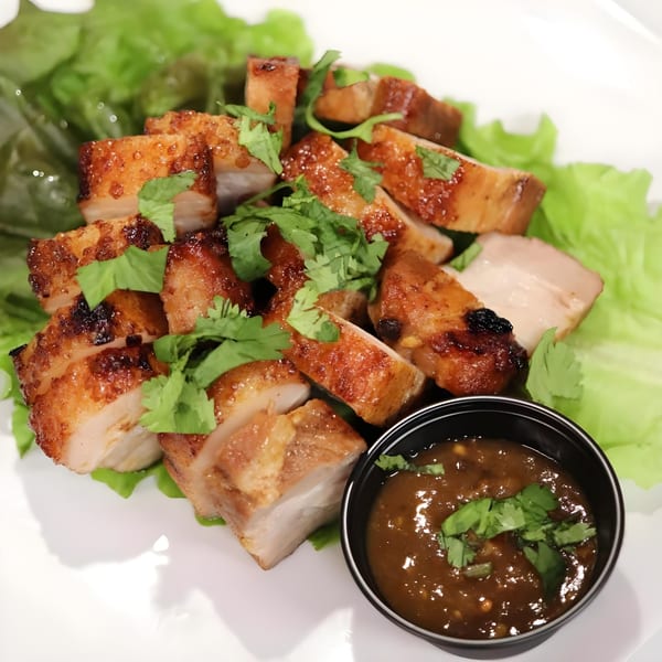 Crispy pork belly slices with cilantro and a side of dipping sauce on a bed of lettuce.