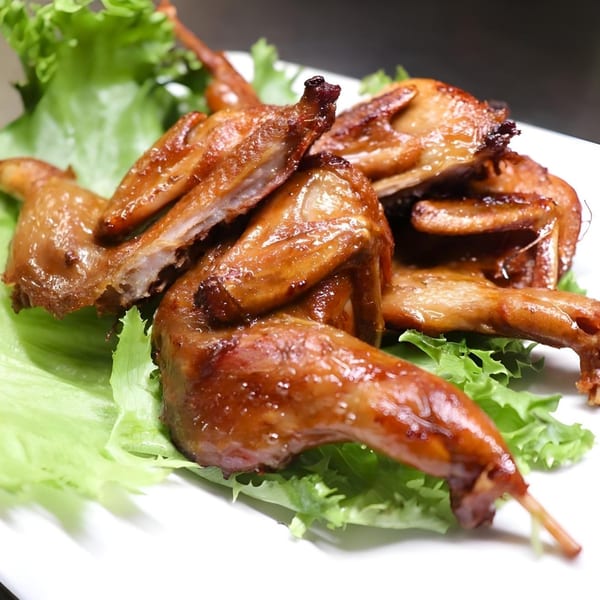 Crispy roasted quail, glazed with a savory sauce, served on a bed of fresh green lettuce.